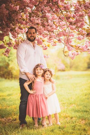 A family portrait under blooming pink cherry blossoms in a sunlit spring garden.