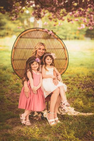 Two children sitting in wicker peacock chairs under pink blossoming trees during golden hour.