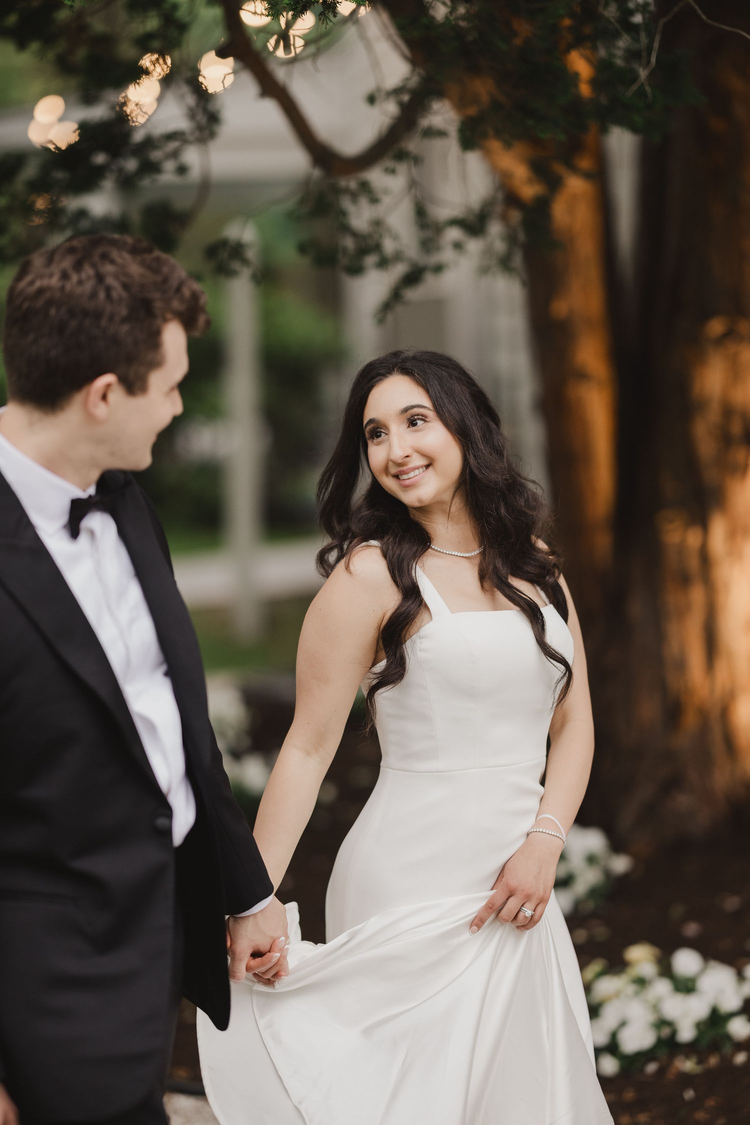 Bride in white gown smiling at groom in black tuxedo during outdoor wedding portrait.
