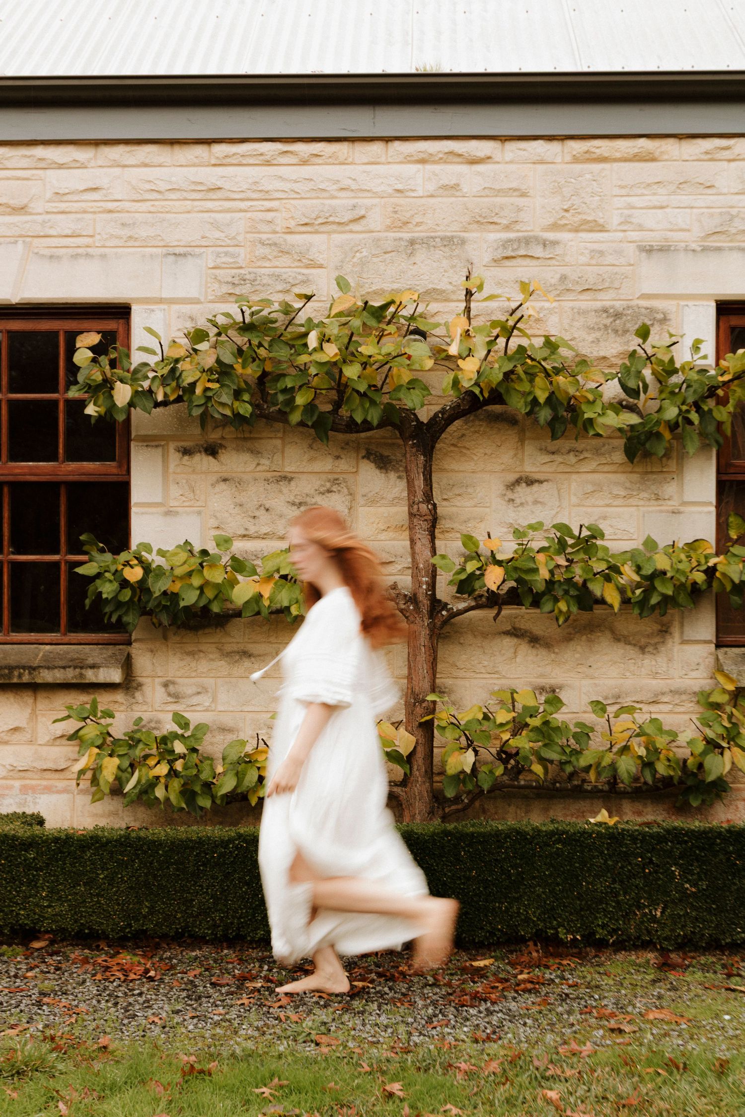A figure in white dress appears to fall and spin across a series of motion-blurred photos against a stone wall backdrop.