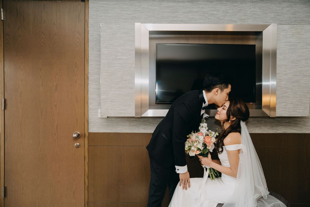 Tender moment between newlyweds with bride in white dress and veil holding floral bouquet.