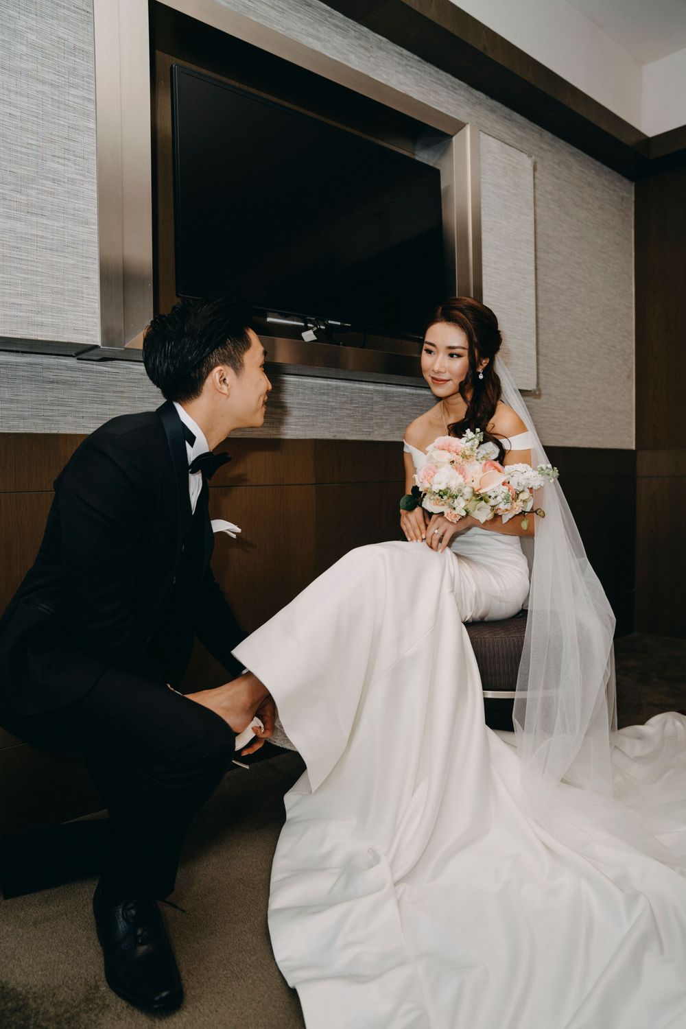 Intimate wedding scene with couple in formal attire seated by modern wall decor.
