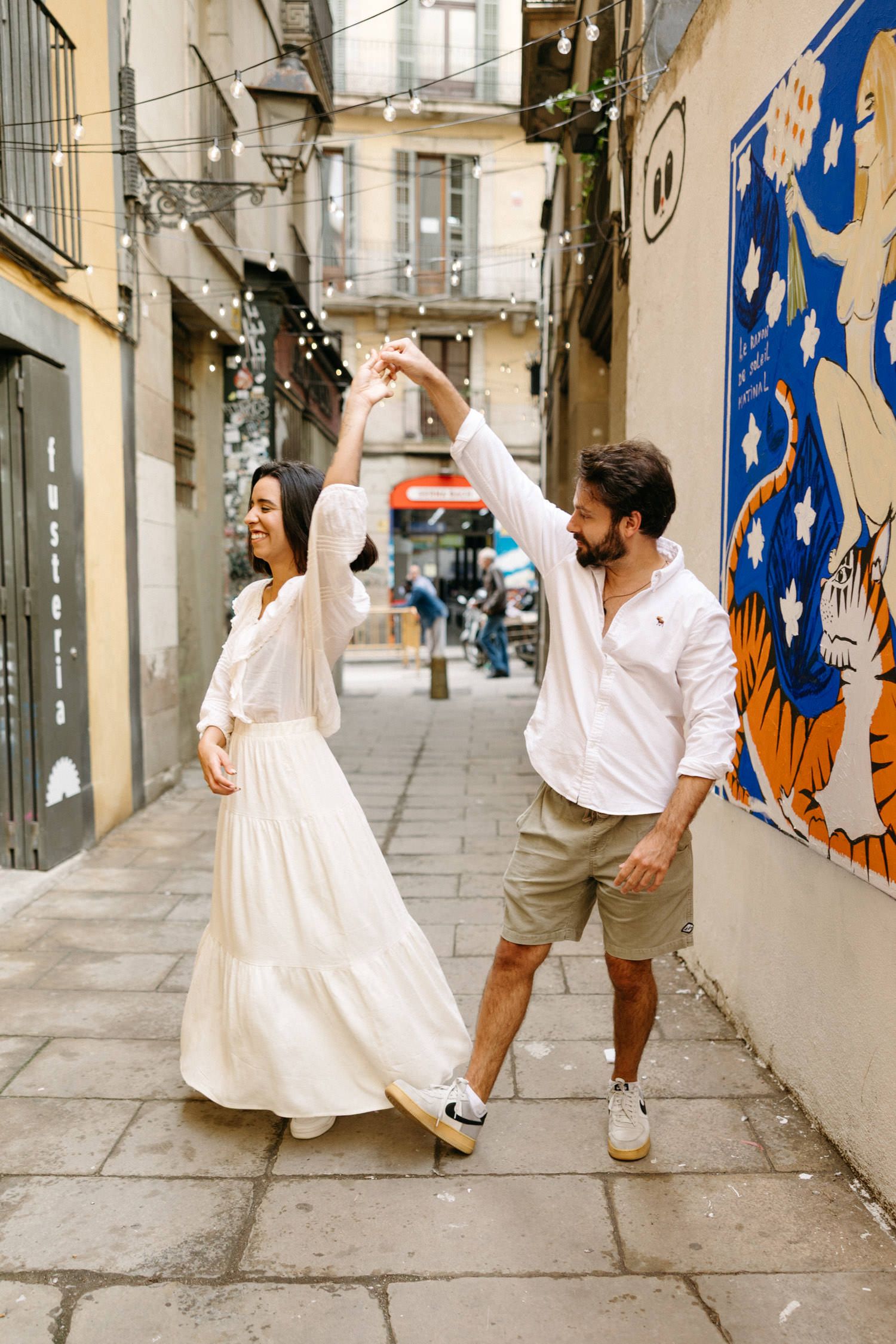 A couple dancing together in a quaint alley decorated with string lights and urban art.