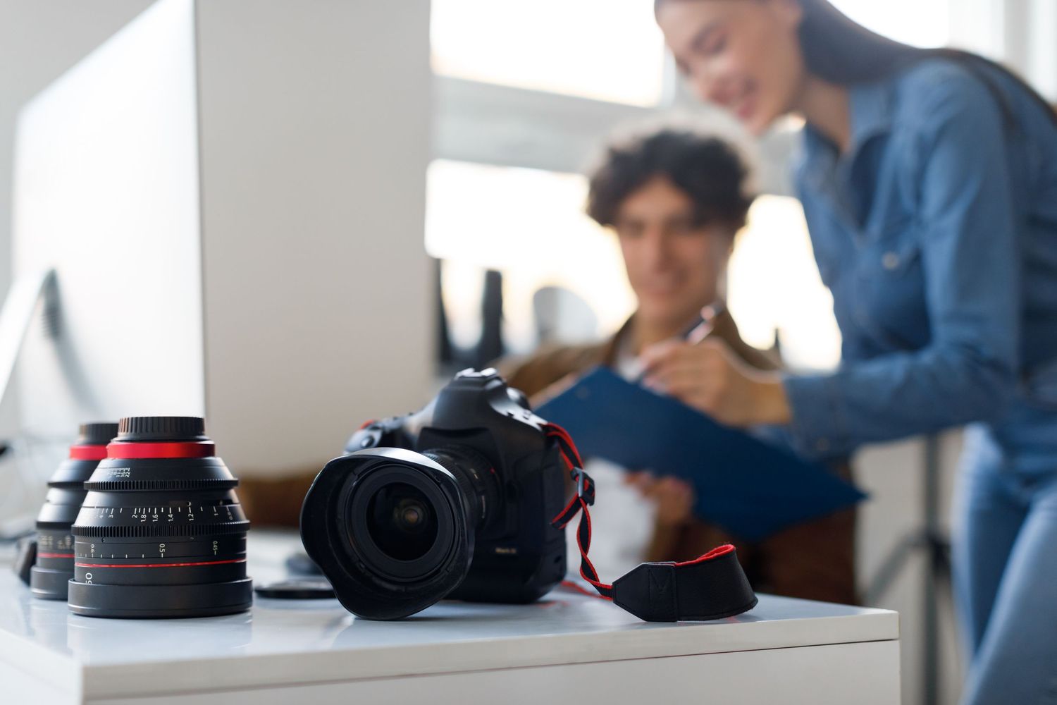 Camera equipment and lenses on a desk while people review photos in the background.