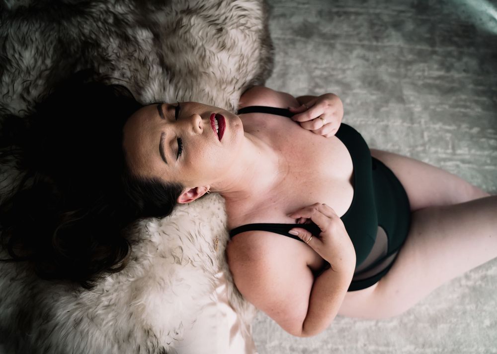 A person in black lingerie lying on a white furry rug in an artistic boudoir photo.