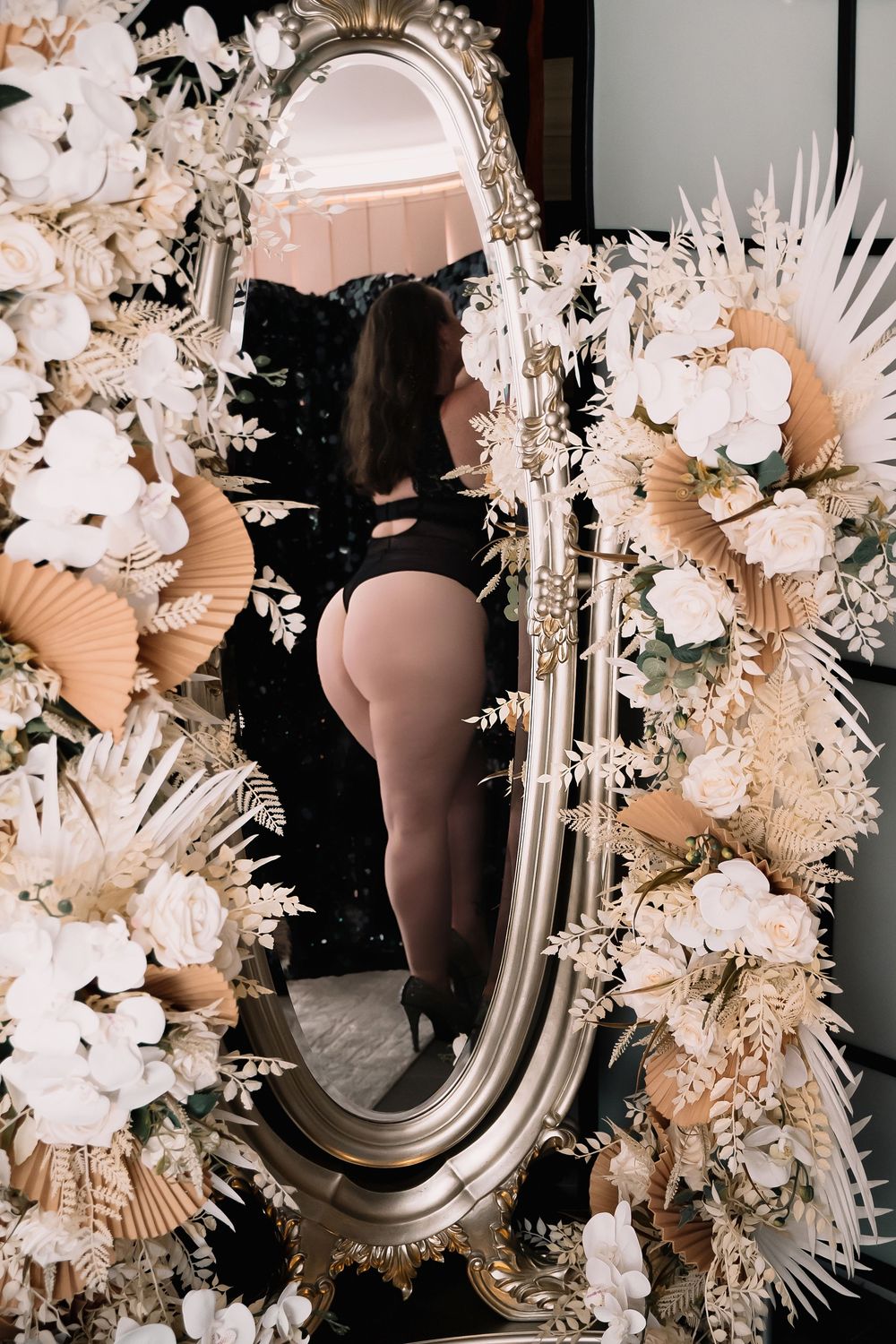 Elegant floral arrangement in blush tones with white flowers and dried palms surrounding an oval mirror makes a statement piece.