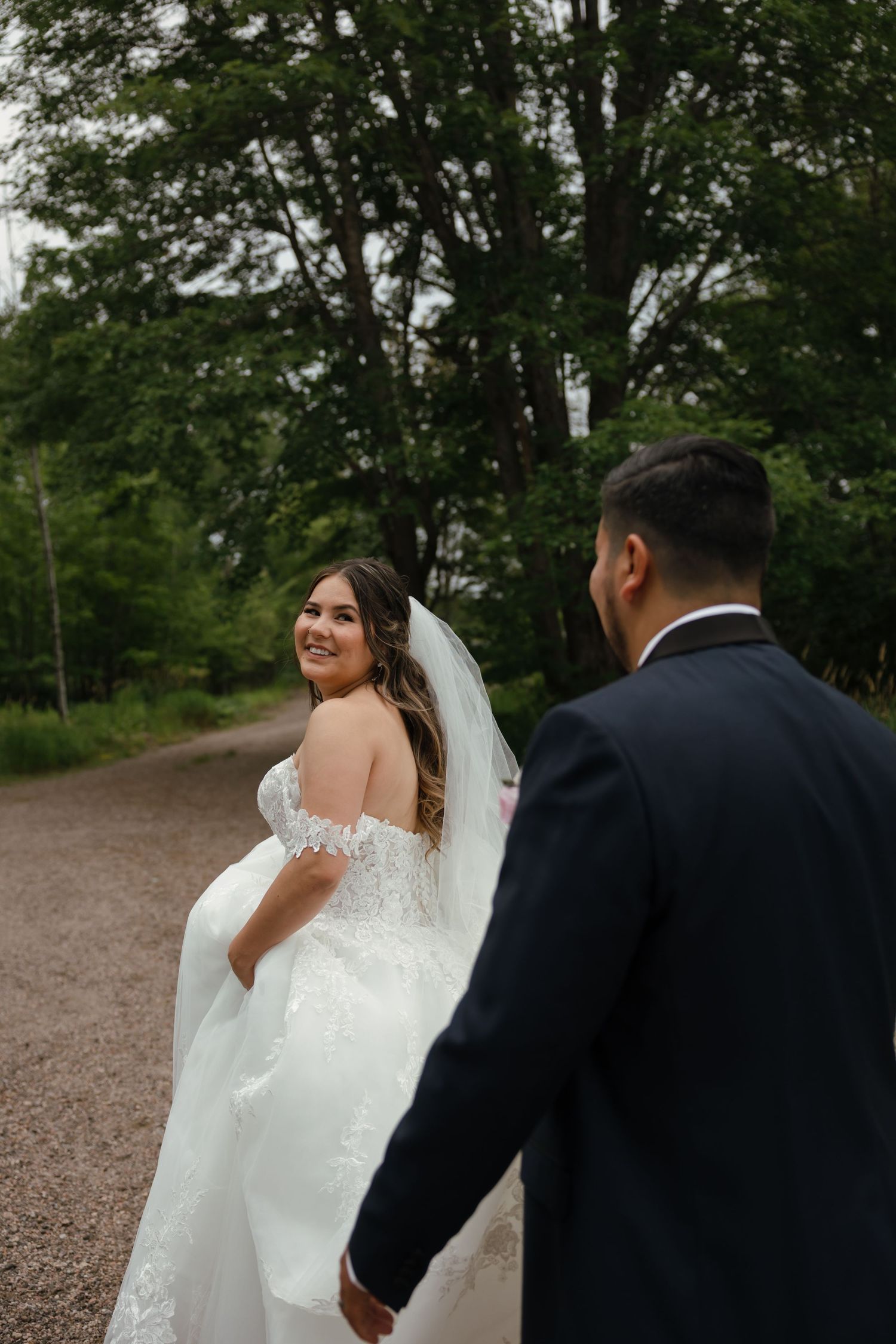 A newly married couple walks along a tree-lined path during their wedding photo session.