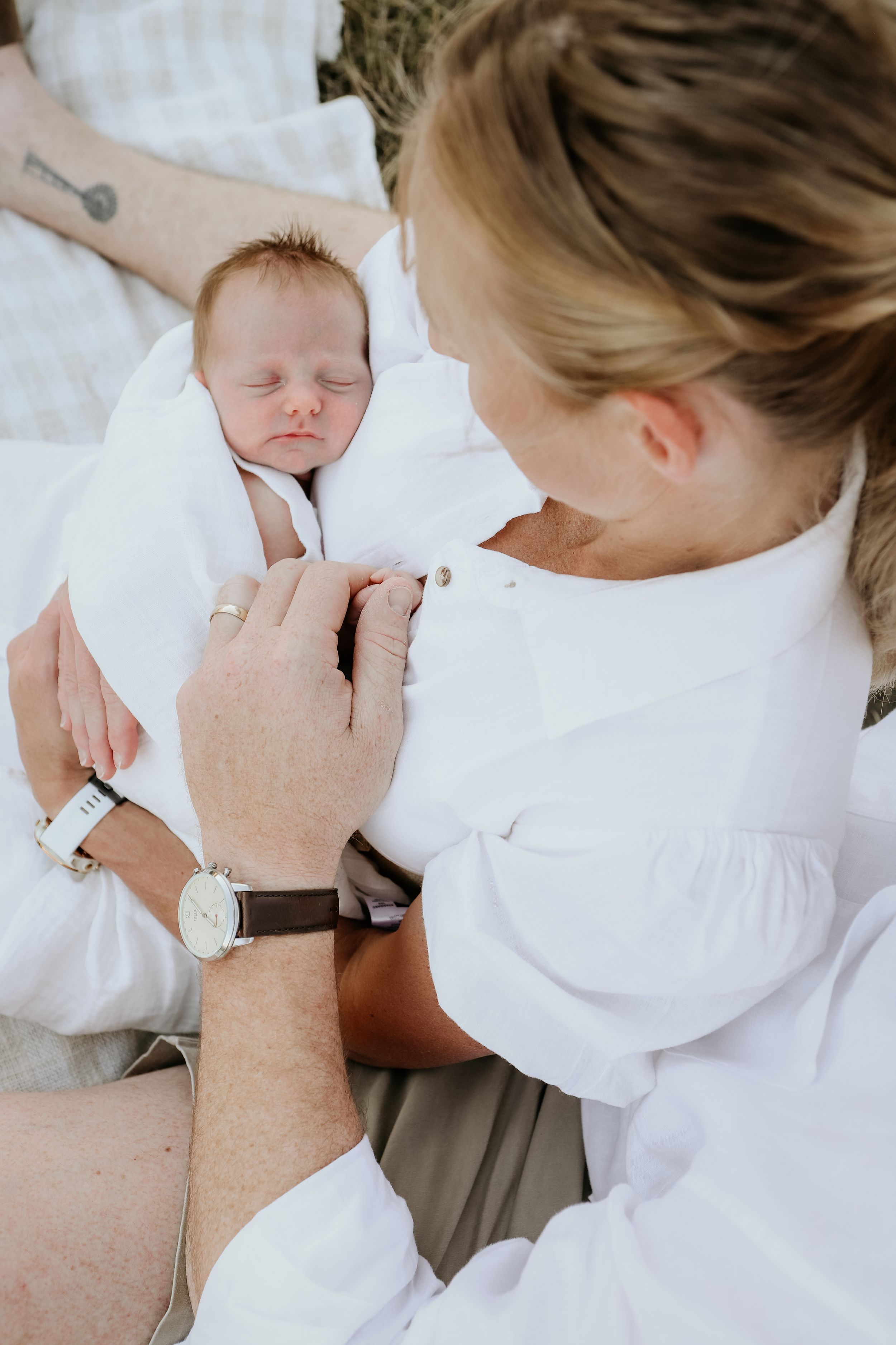 Close-up series of tender moments between parent and baby wearing white clothing on white bedding.