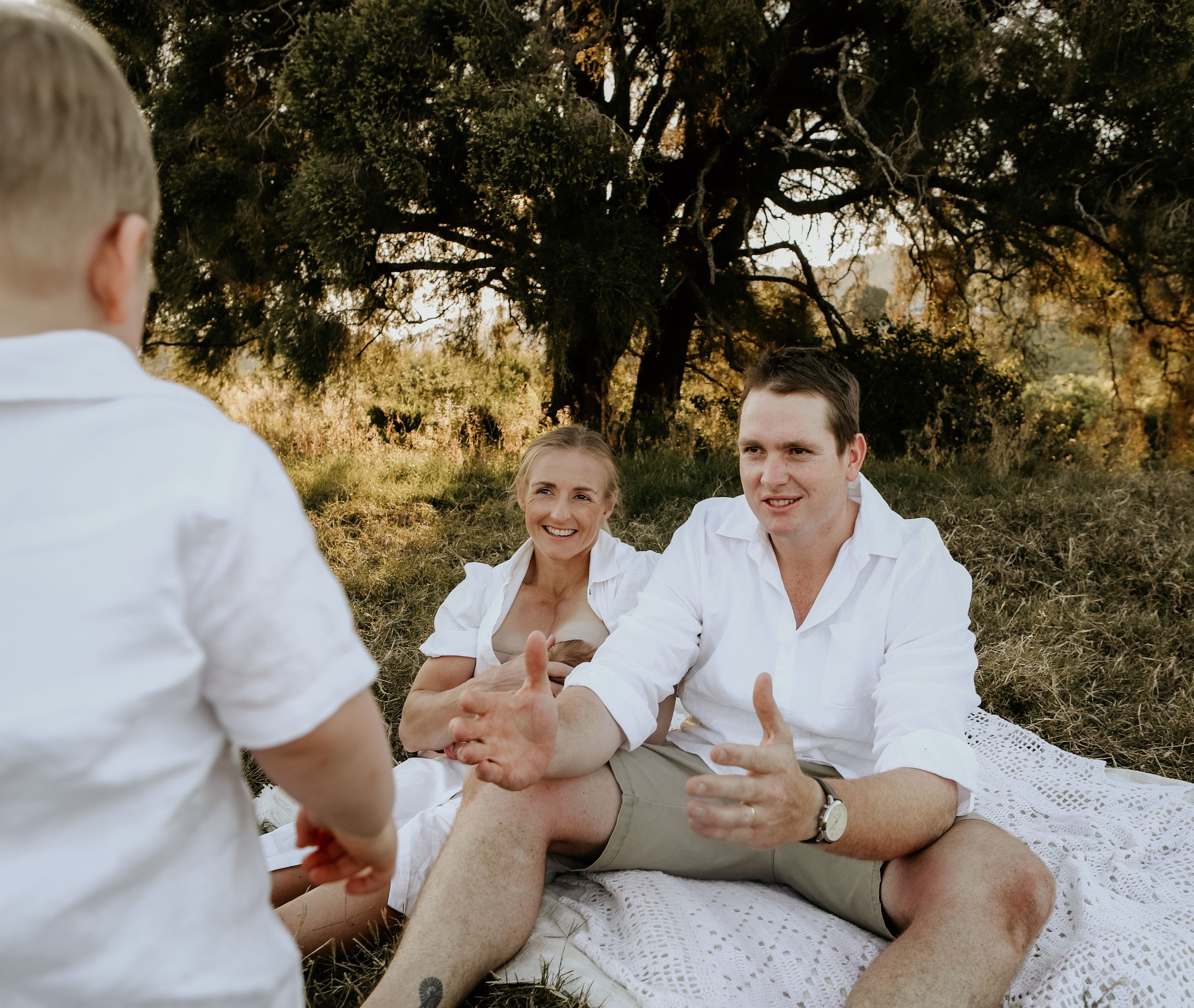 A group in white clothing sits together on a blanket in a sunny outdoor setting, sharing joyful moments together.