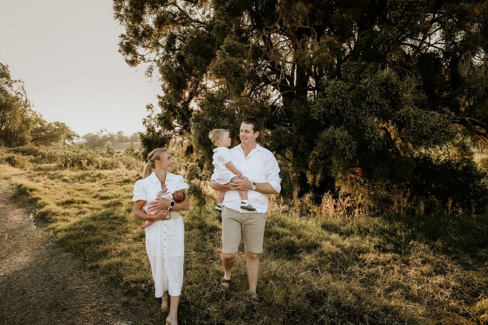A couple in white outfits poses together during a golden hour outdoor photoshoot in a rustic natural setting.