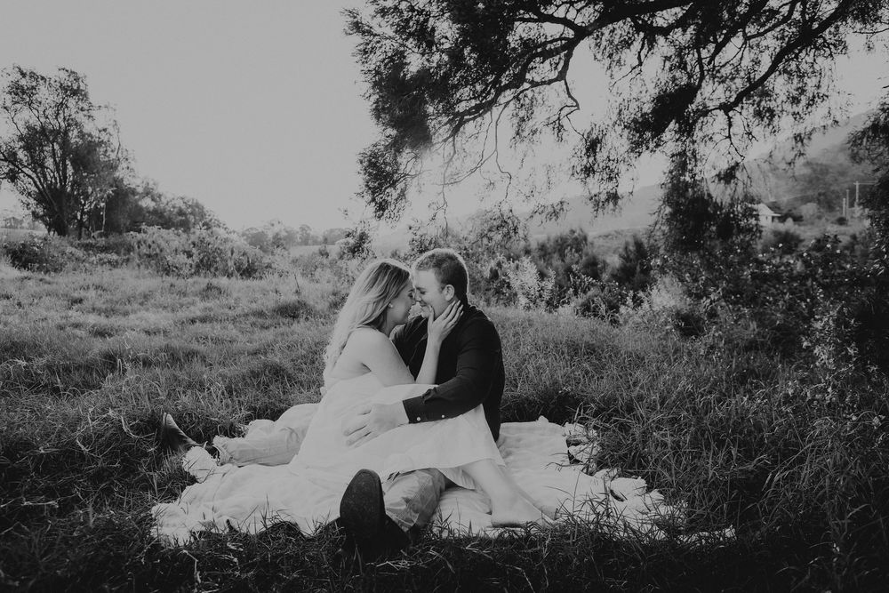 A romantic black and white photograph of a couple sitting on a blanket in a dreamy outdoor setting.