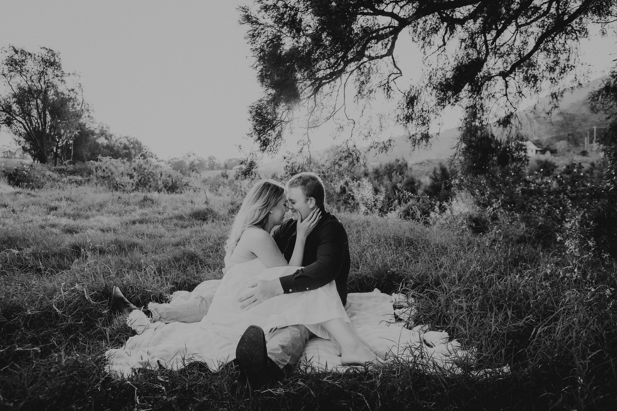 A romantic black and white photograph of a couple sitting on a blanket in a dreamy outdoor setting.