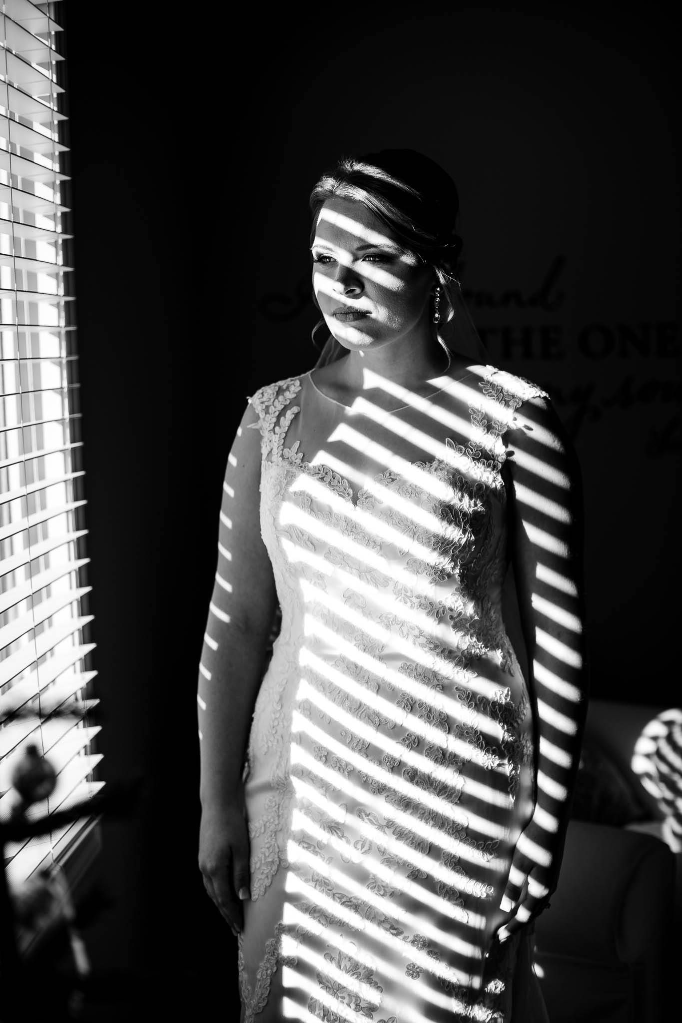 Black and white artistic photo showing shadows of window blinds creating dramatic striped patterns on a figure.