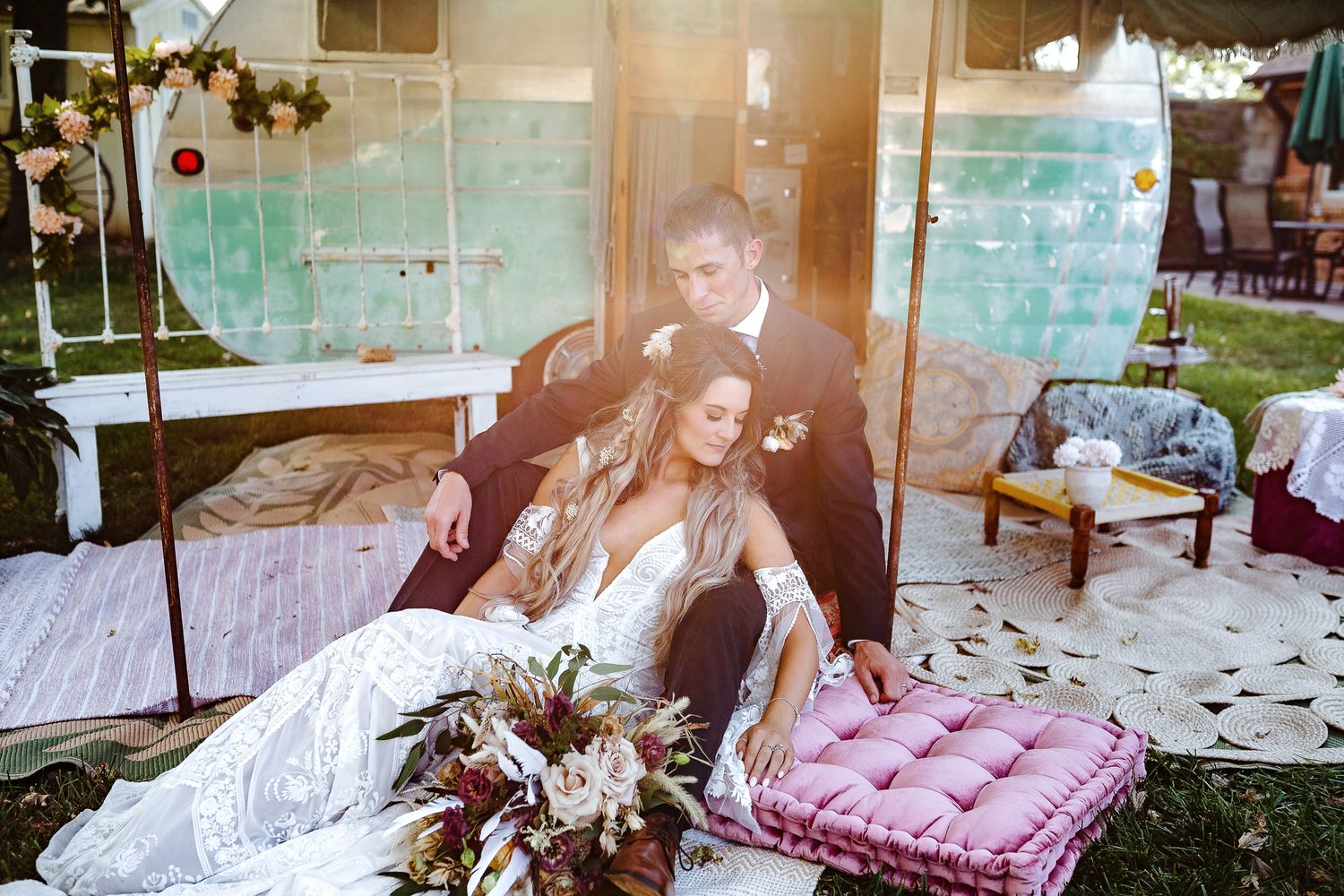 Artistic wedding portrait with couple lounging on floor with boho decor and teal wall backdrop.