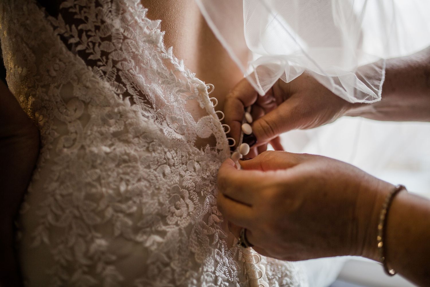 Close-up detail shots of a delicate lace wedding dress being fastened with tiny buttons and hooks.