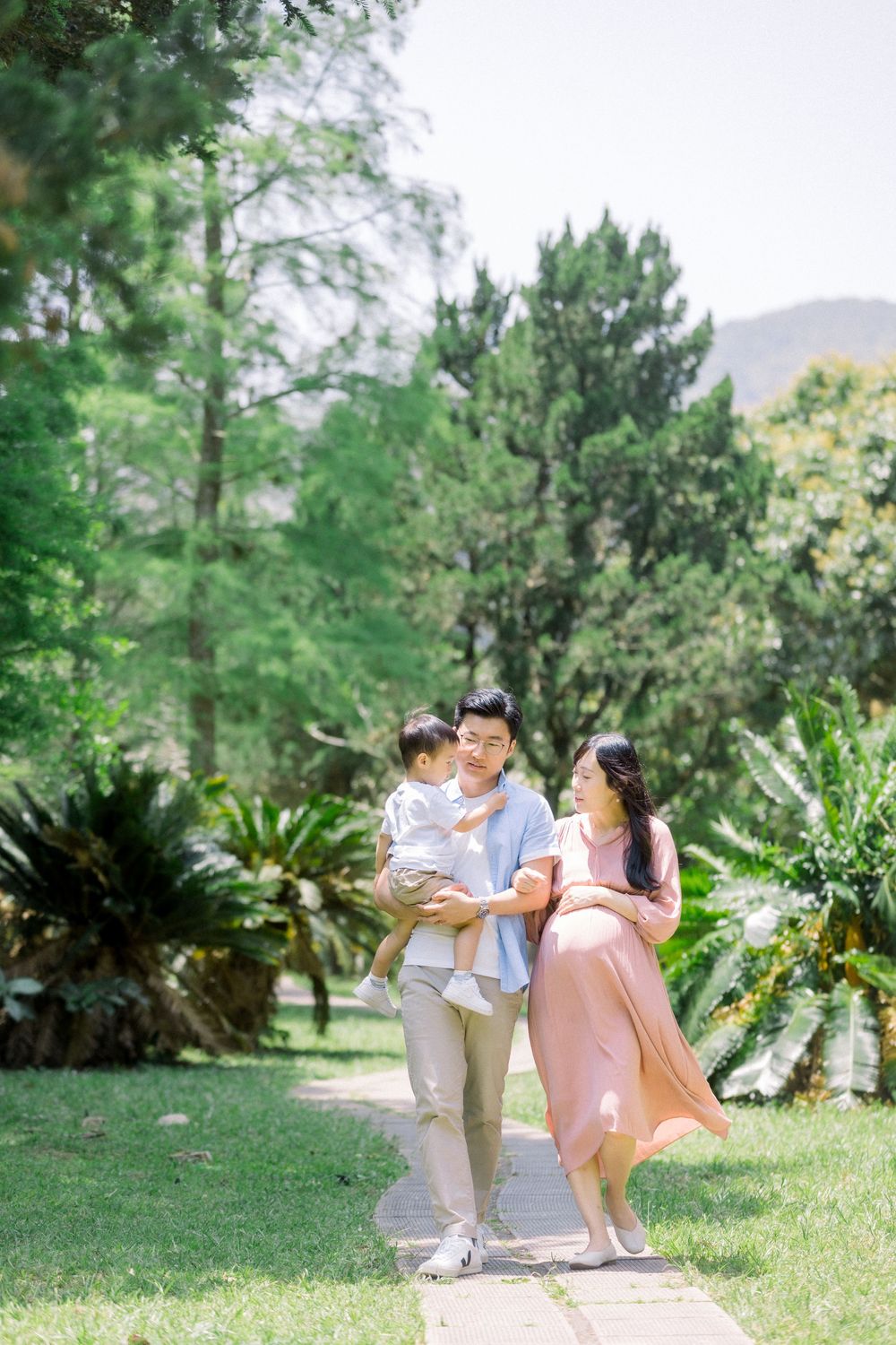 A couple shares tender moments together in a lush garden setting with pine trees and greenery in the background.
