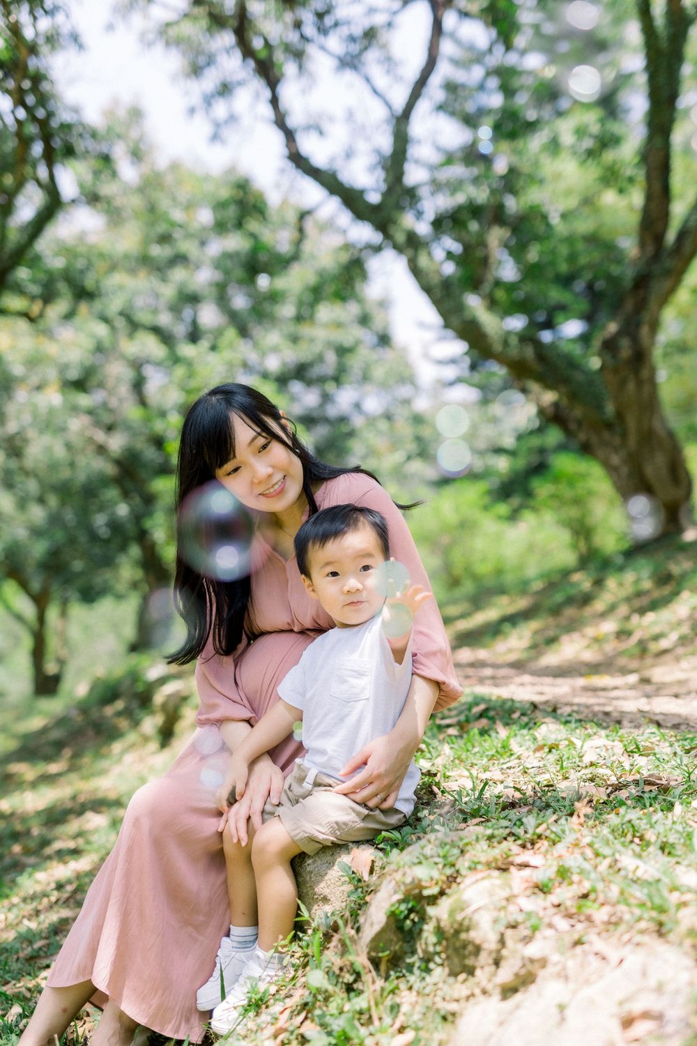 Mother and child share tender moments together on a grassy hillside in a sunlit forest setting.