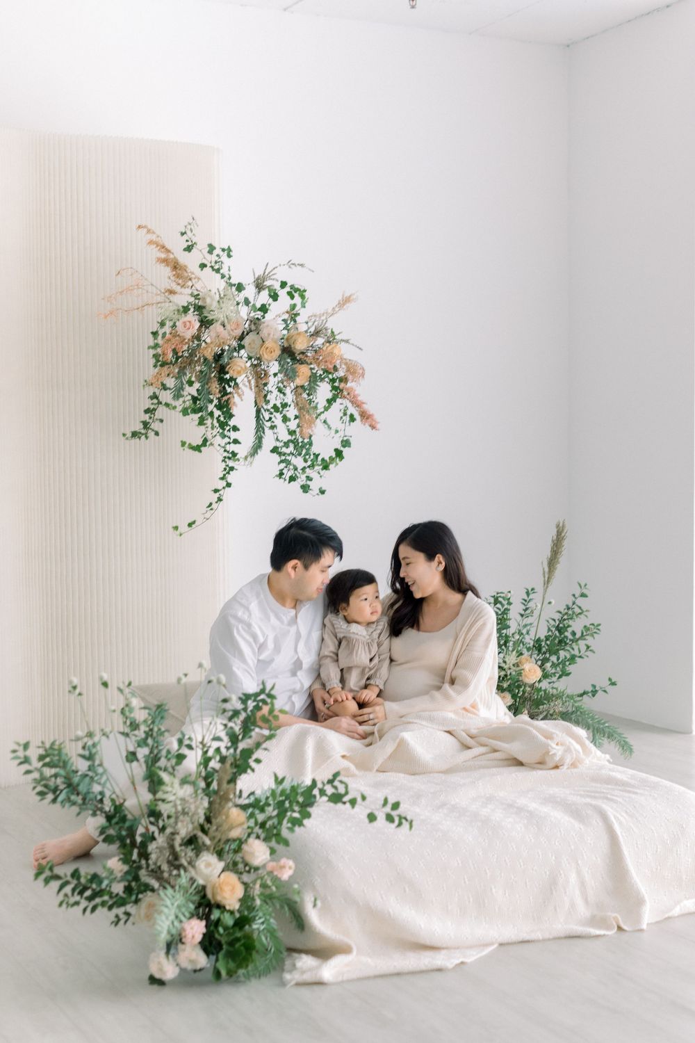 A minimalist white bedroom scene with elegant floral arrangements featuring eucalyptus and peach-colored blooms.