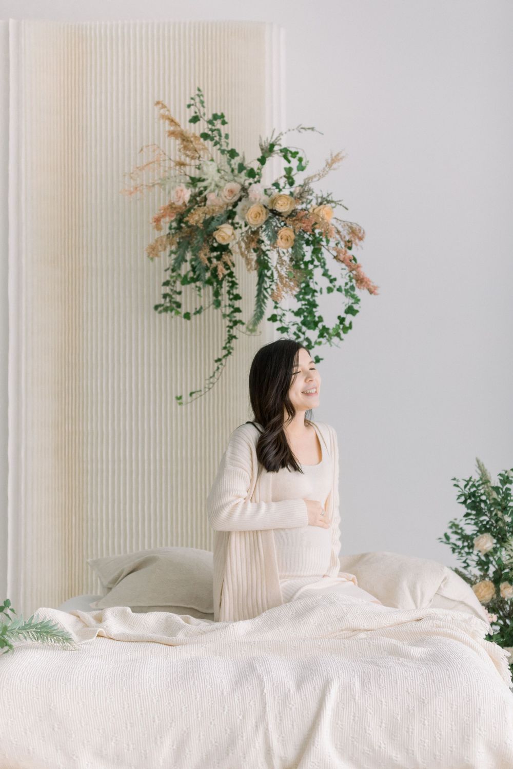 Ethereal series of photos showing a figure in white bedding with delicate floral arrangements against a light wall.