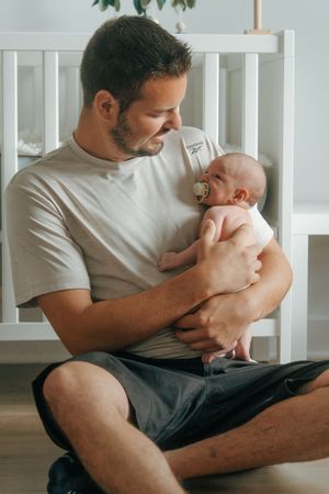 A parent in a white t-shirt tenderly holds and cuddles with a newborn baby in a home setting.