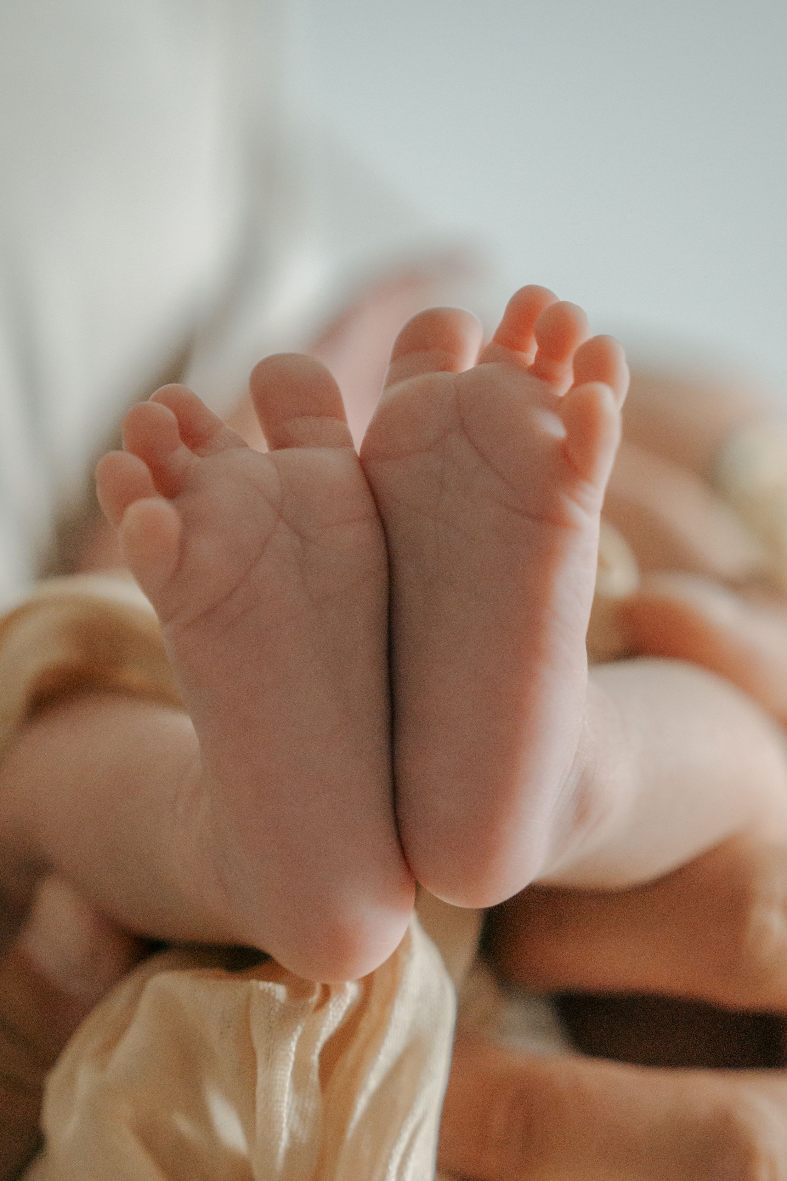 Close-up shot of tiny baby feet with delicate wrinkled soles resting on soft cream-colored fabric.