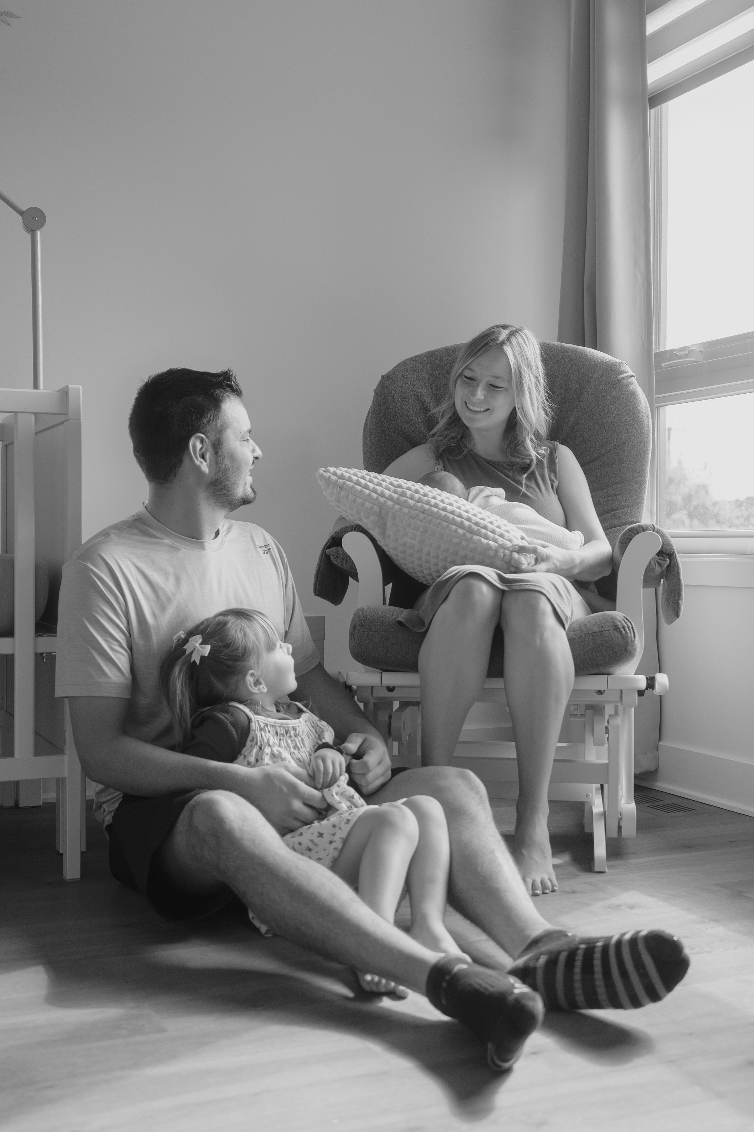 Black and white photo series showing a family relaxing together in an empty room with sunlight streaming through windows.