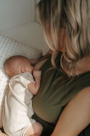 A sleeping infant rests peacefully against someone's shoulder while natural light streams in from the window.
