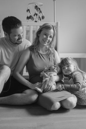 Black and white photos showing intimate family moments with a baby on a hardwood floor.