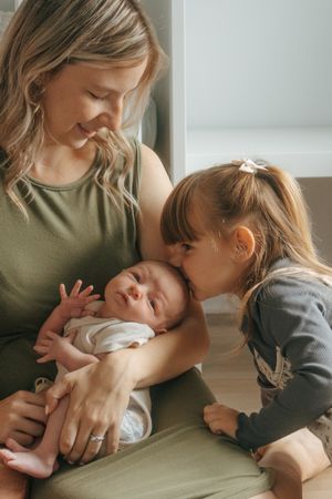 Intimate family moment as siblings bond with newborn baby in a series of candid indoor photos.