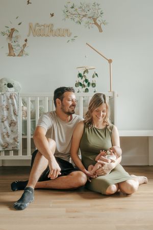A couple relaxes together on a hardwood floor in a nursery room with decorative wall decals.