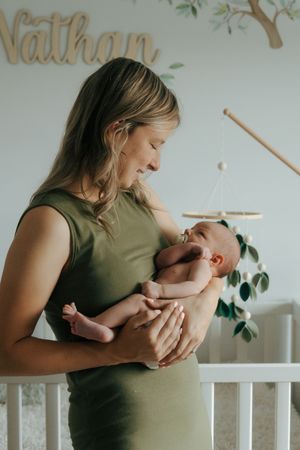 Woman in olive green top cradles newborn baby in set of four tender moments by nursery crib.