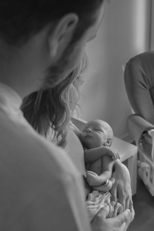A tender black and white portrait of someone lovingly holding a tiny newborn baby in their arms.