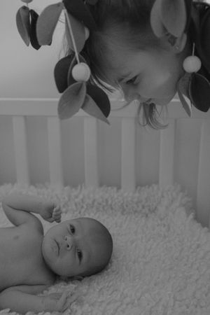 Black and white portrait of baby lying on textured blanket beneath foliage decoration.