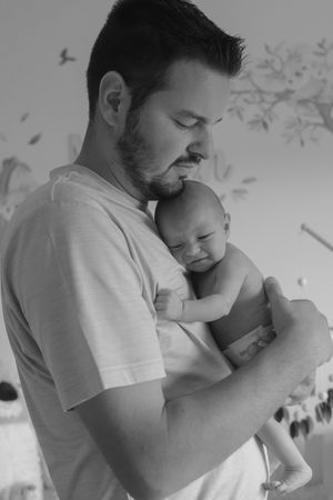 Series of monochrome photos capturing intimate moments between a father and baby in a nursery.