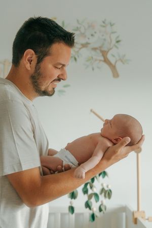 Collection of photos showing a father cradling and bonding with newborn against light wall with tree decals.