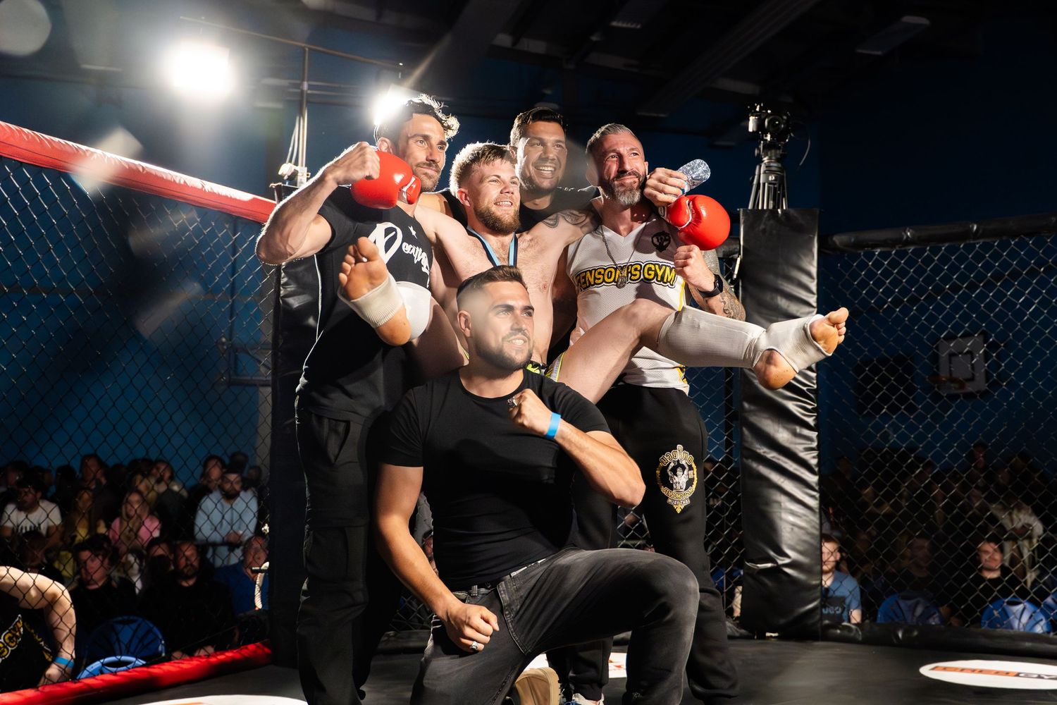 A victorious celebration moment in the MMA octagon as a group lifts their champion in triumph.