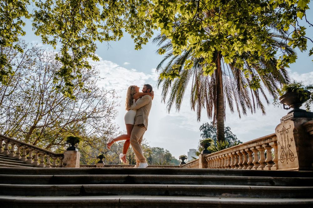 Couple holding hands tenderly along a tree-lined path.