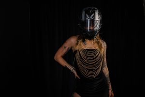 Dramatic portrait of performer in metal mask and chains against dark background.