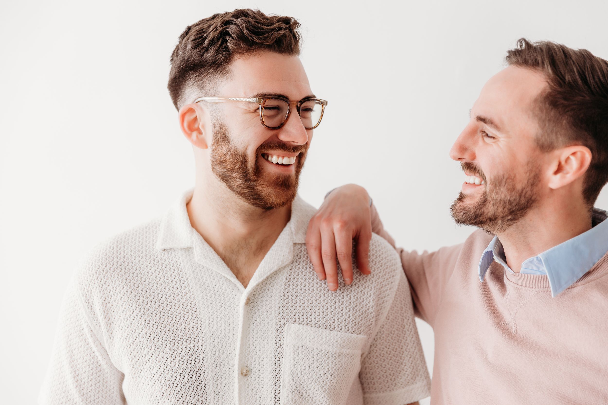 Two men in casual attire share genuine laughter against white background.