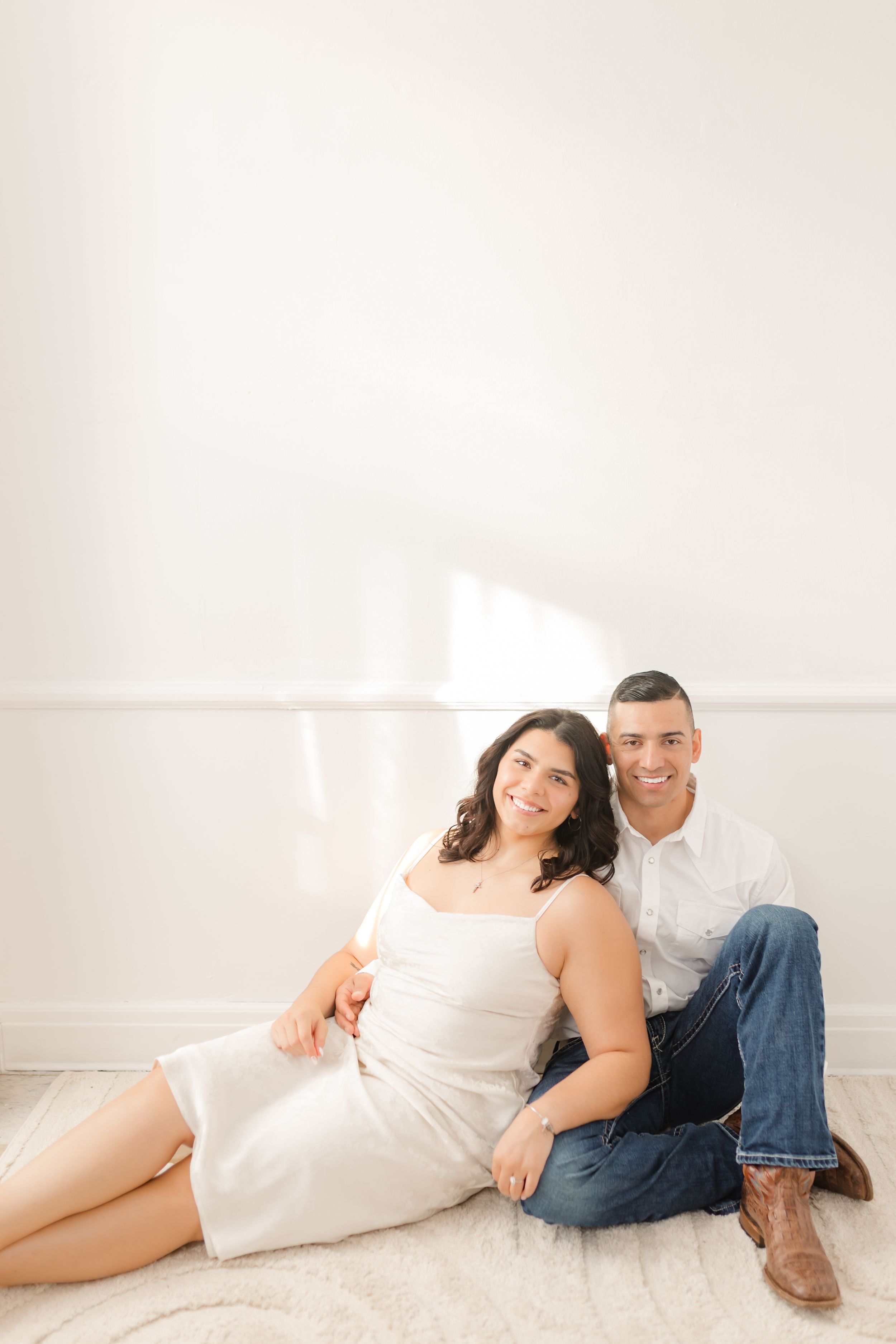 A couple in white and denim lounges together in a bright minimalist setting creating intimate portraits.