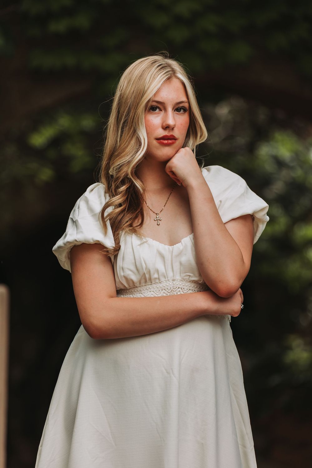 A person in a white dress strikes different contemplative poses outdoors against a dark green foliage background.