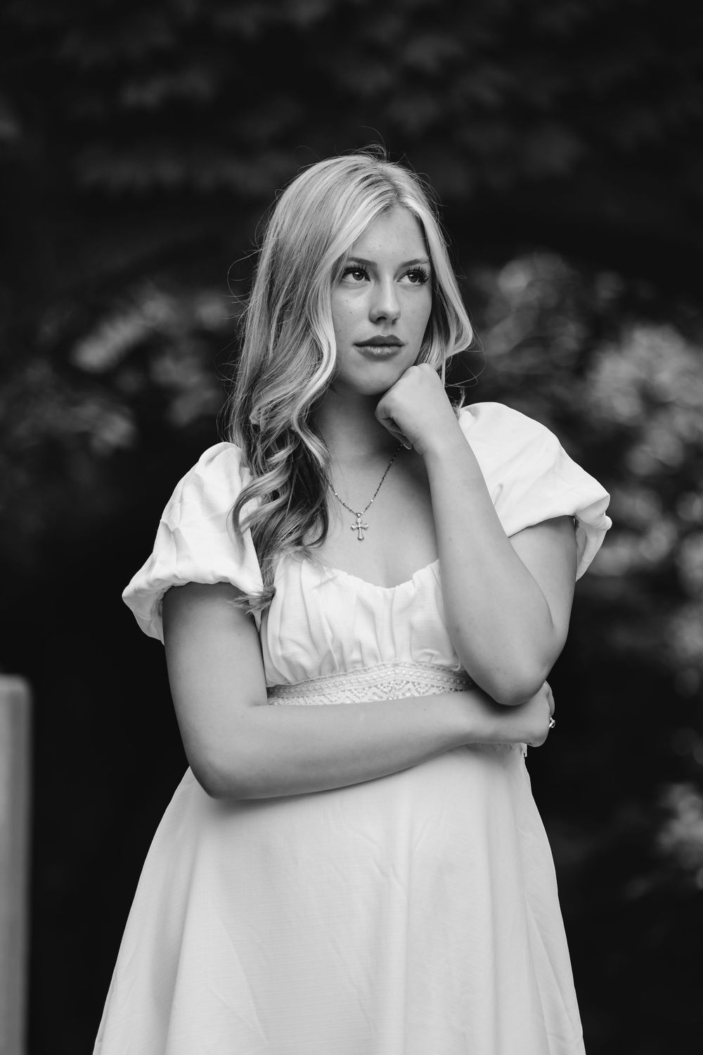 A woman in a white dress poses thoughtfully against a dark background in an artistic black and white portrait series.