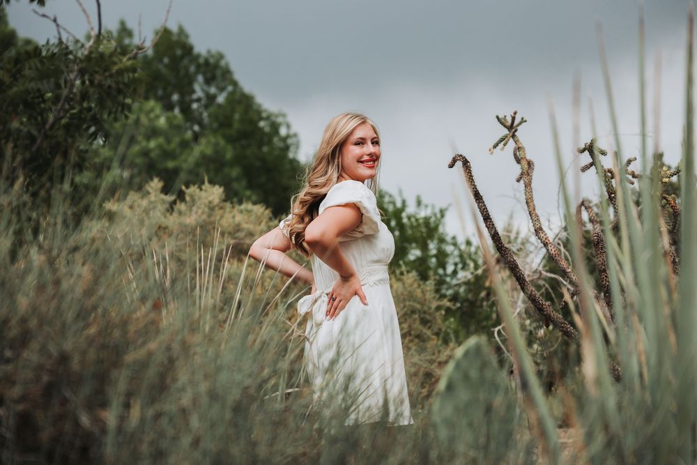 A woman in a white dress dances joyfully in a field of tall grass and wildflowers at sunset.