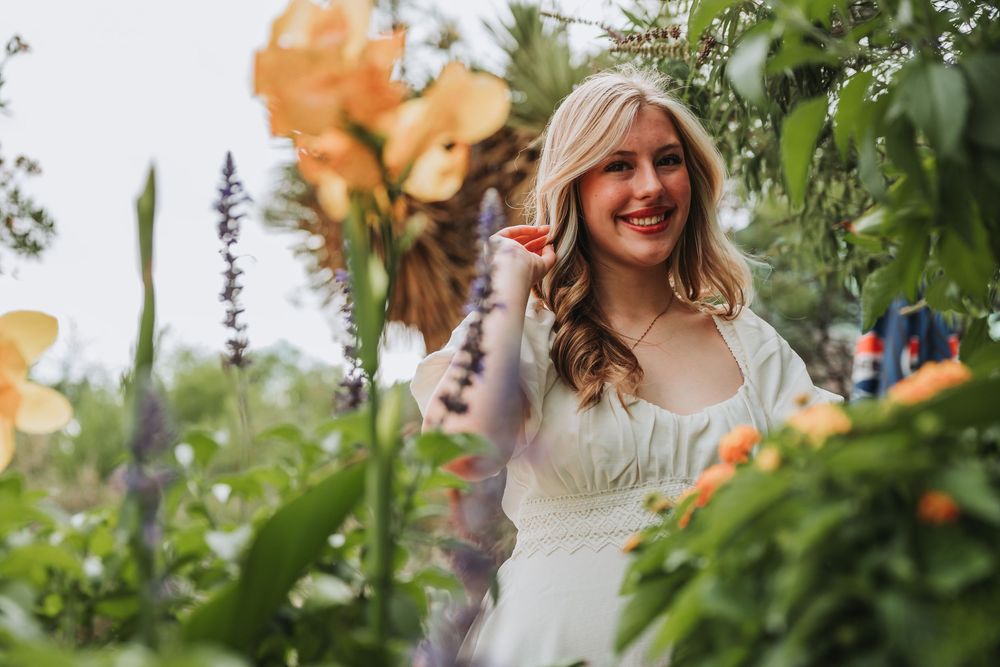 Woman smiling in a garden setting surrounded by orange butterfly decorations and greenery.