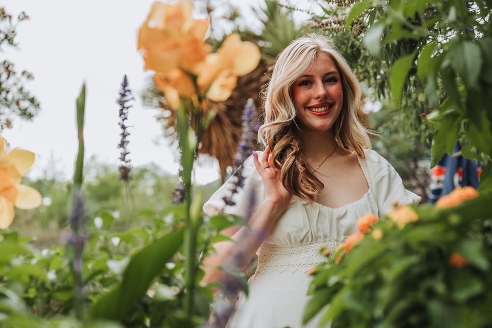 Woman smiling in a garden setting surrounded by orange butterfly decorations and greenery.