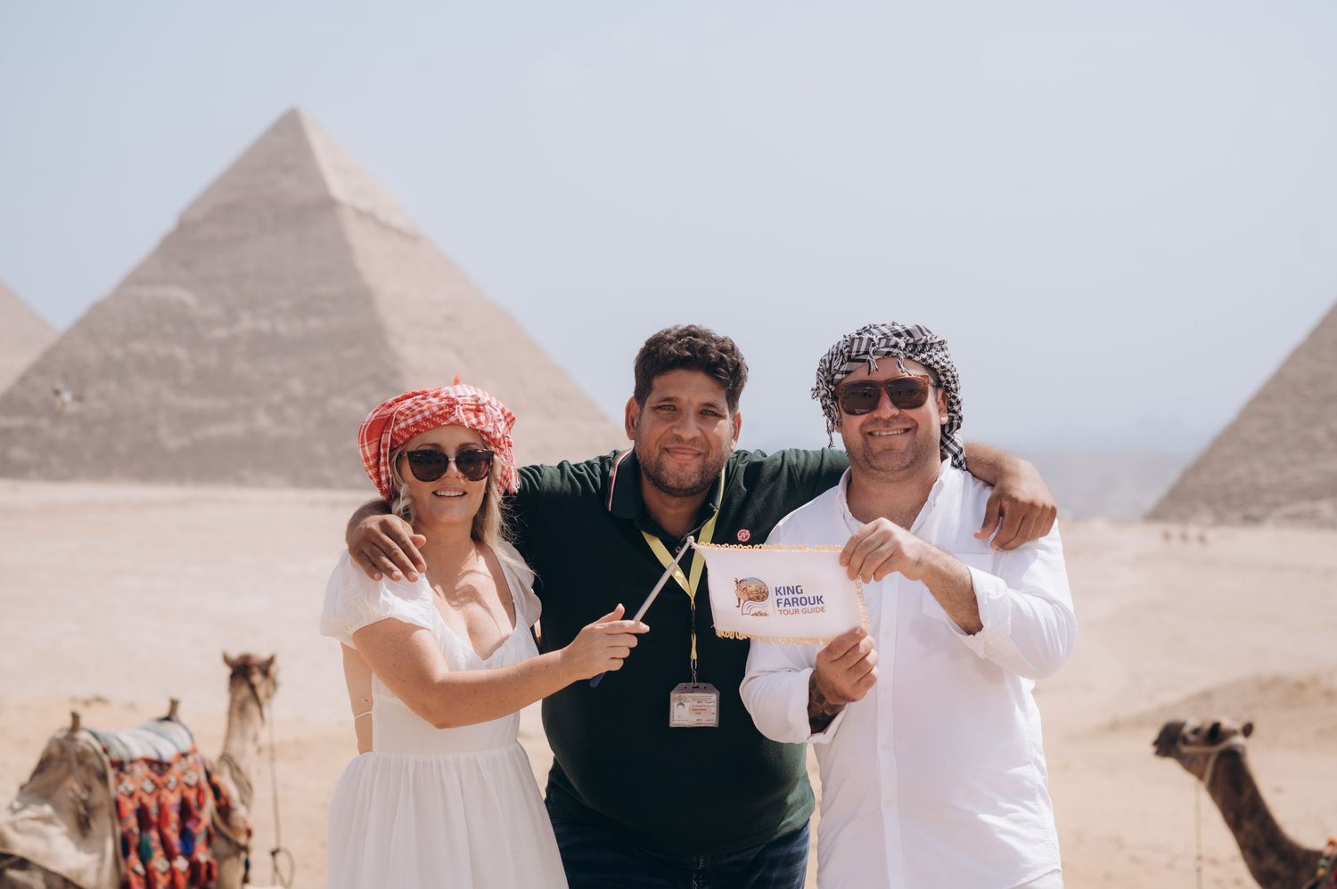 Tourists pose with gestures in front of the iconic pyramids of Giza with camels in background.