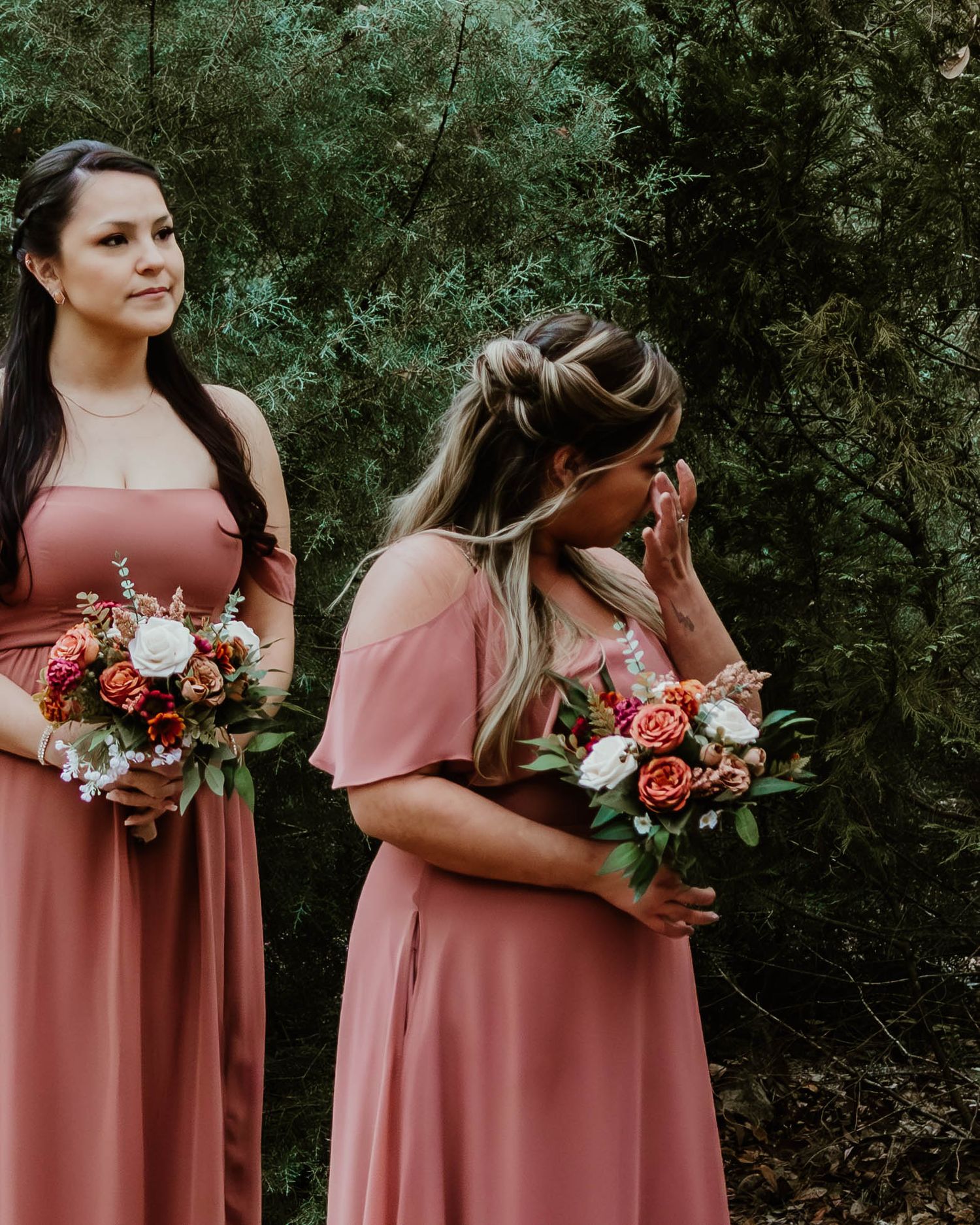 Row of bridesmaids in matching dusty rose dresses holding floral bouquets against green foliage. Timeless wedding photography Florida