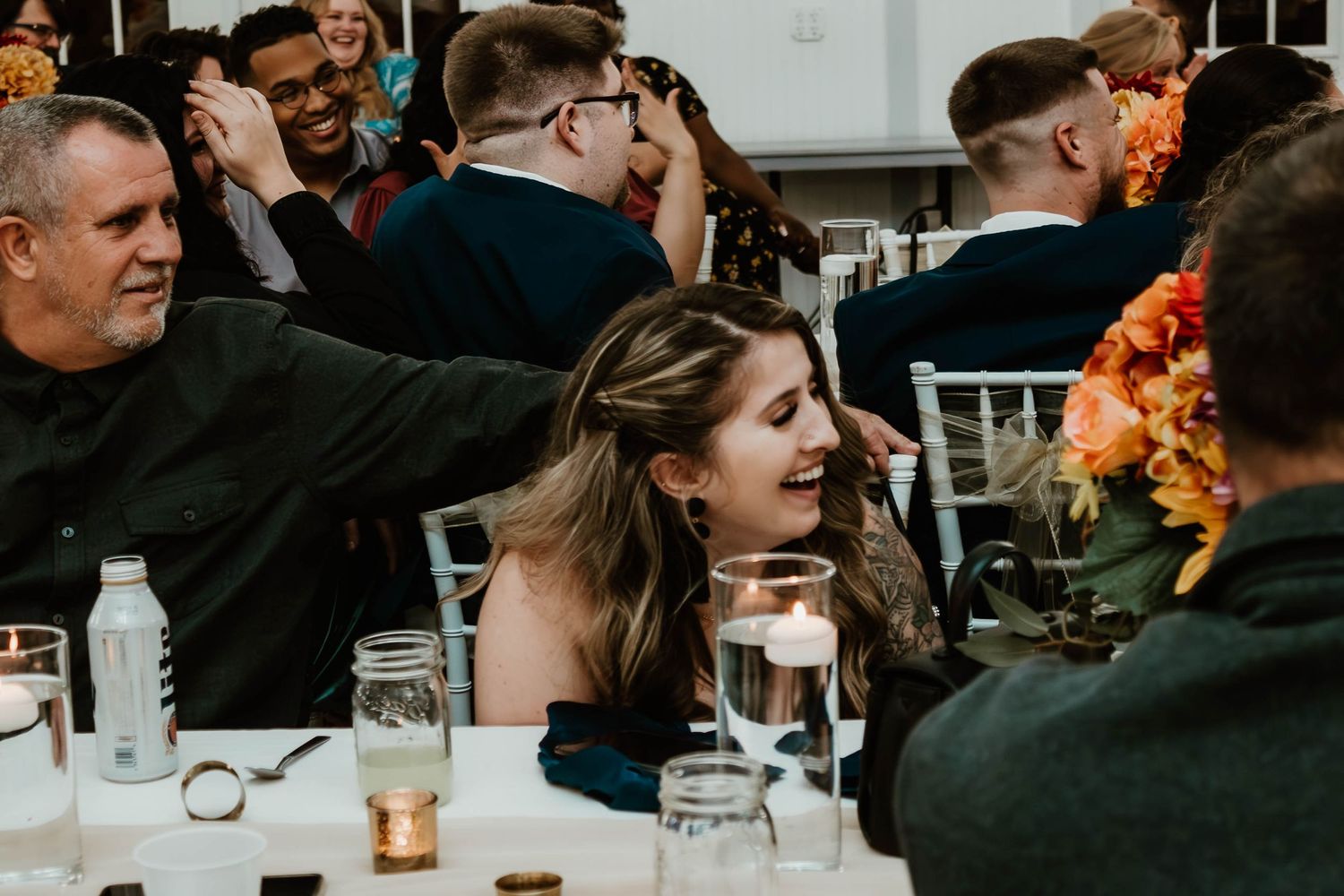 Guests converse at tables during an evening reception with glowing candlelight and mason jar decorations. fun candid wedding photos Florida