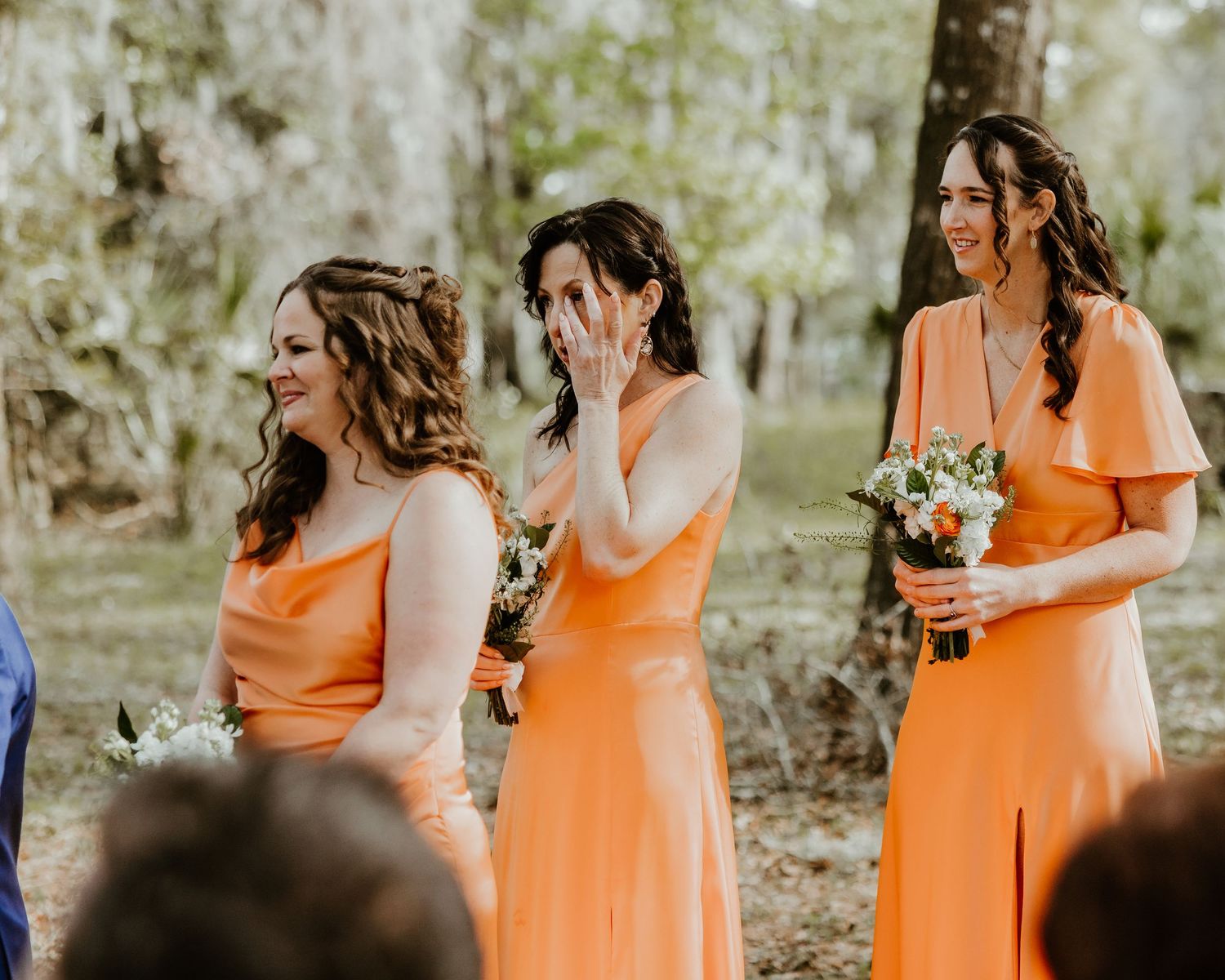 Emotional reactions from bridesmaids wearing coral orange dresses during an outdoor wedding ceremony. editorial wedding photos