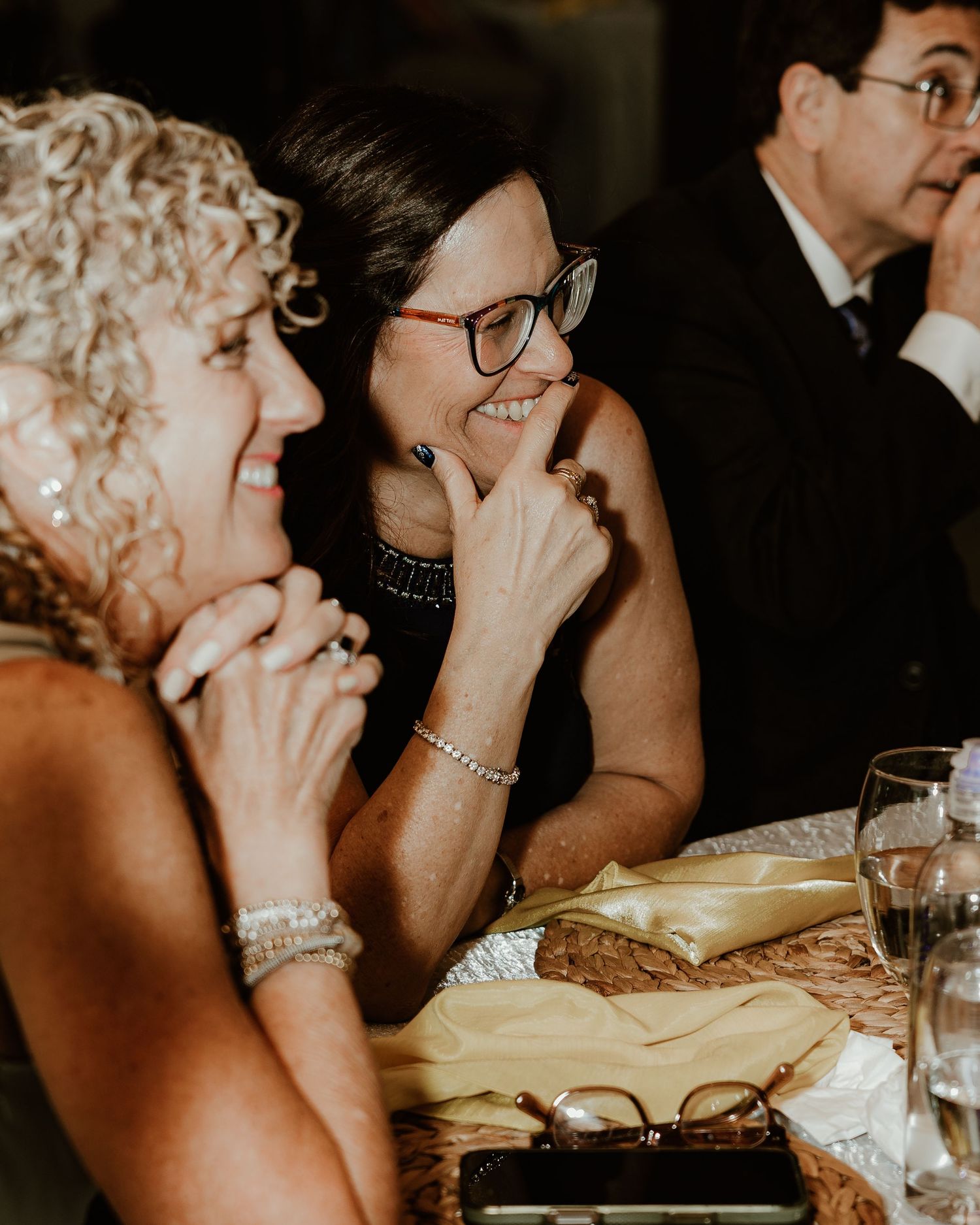 Guests laughing and sharing emotional moments during a formal dinner event in a dimly lit setting. wedding reception. Tampa wedding photos